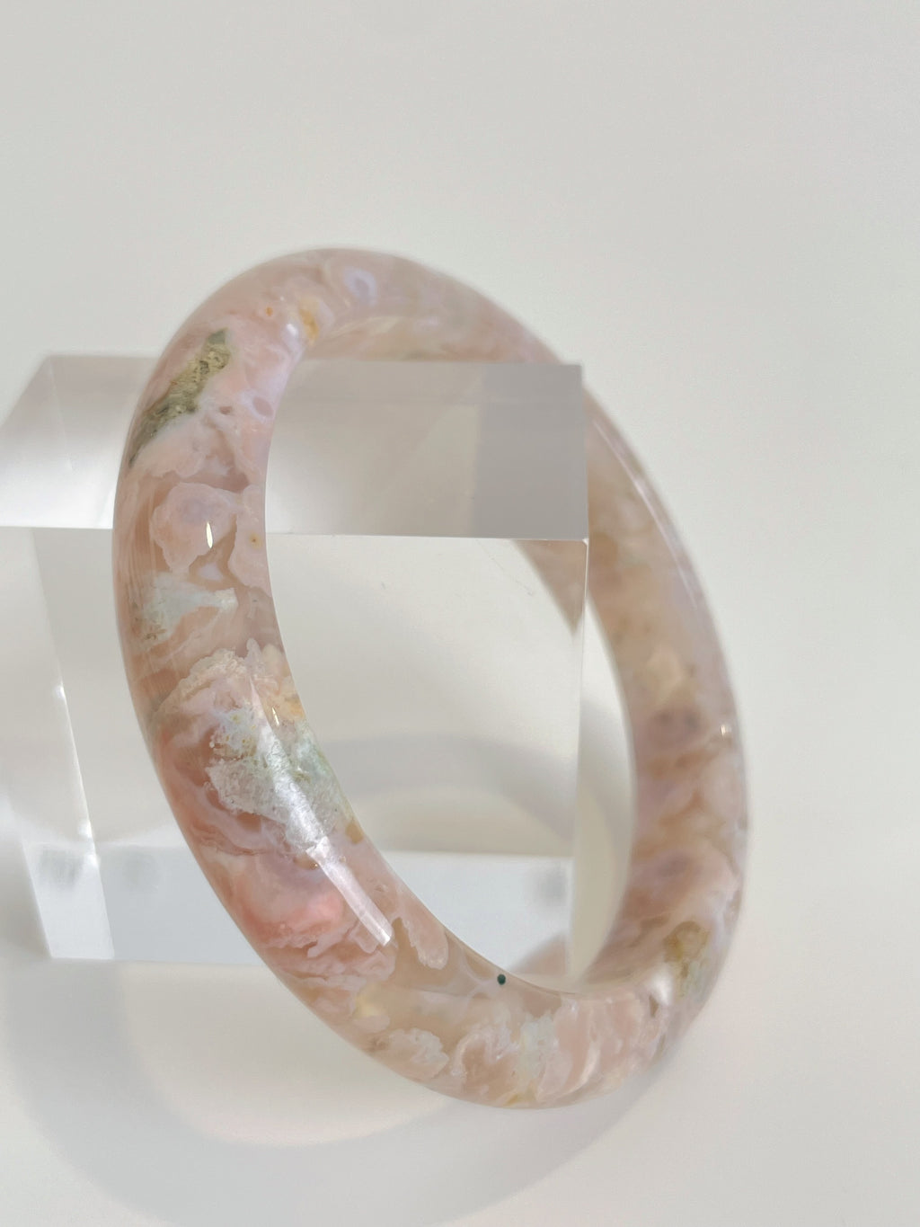 Beautiful flower agate bangle showcasing soft pink hues and floral patterns, displayed on a clear stand.