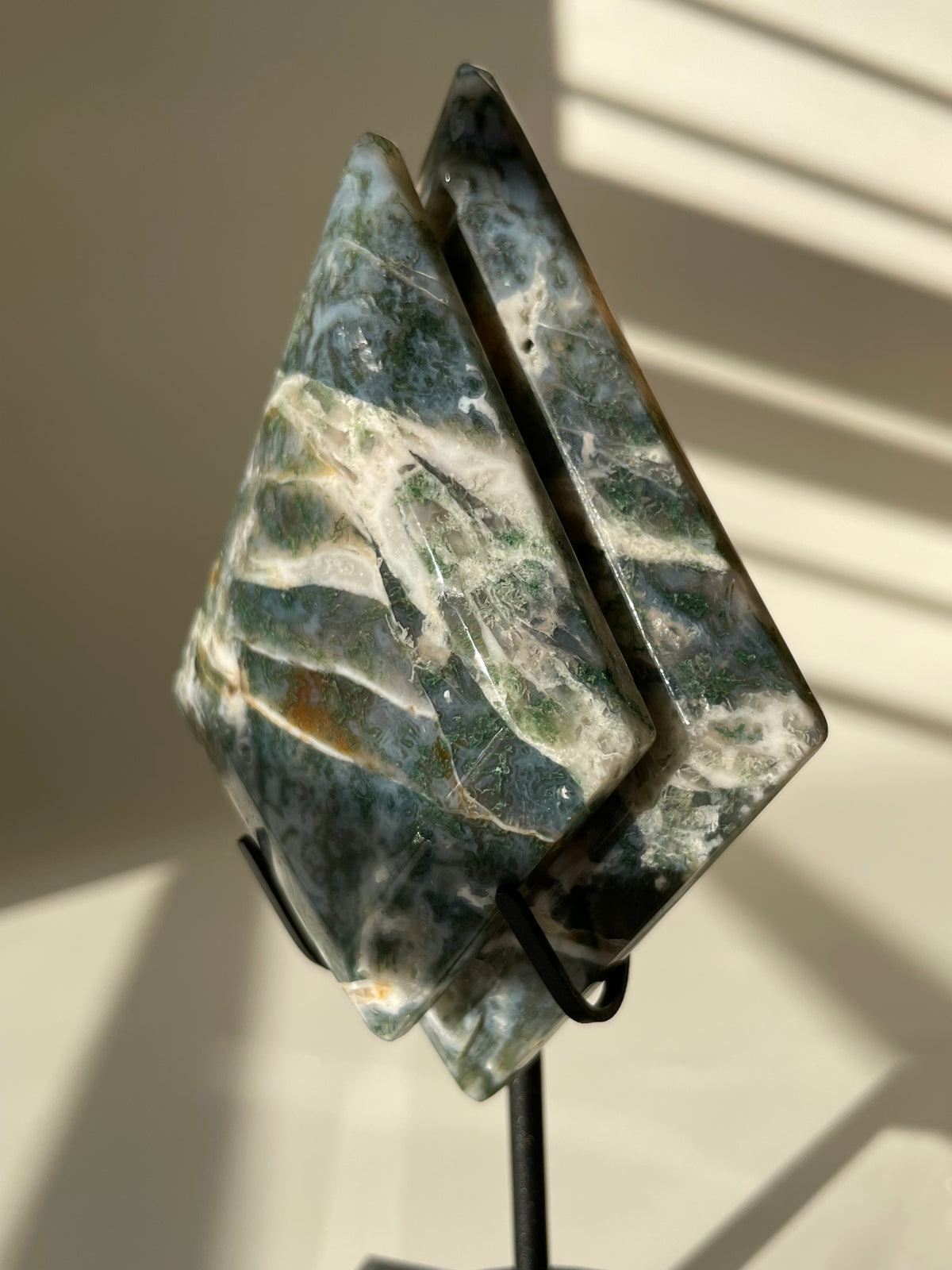 Scenic moss agate specimen displayed on a black stand, showcasing its unique green and white patterns.