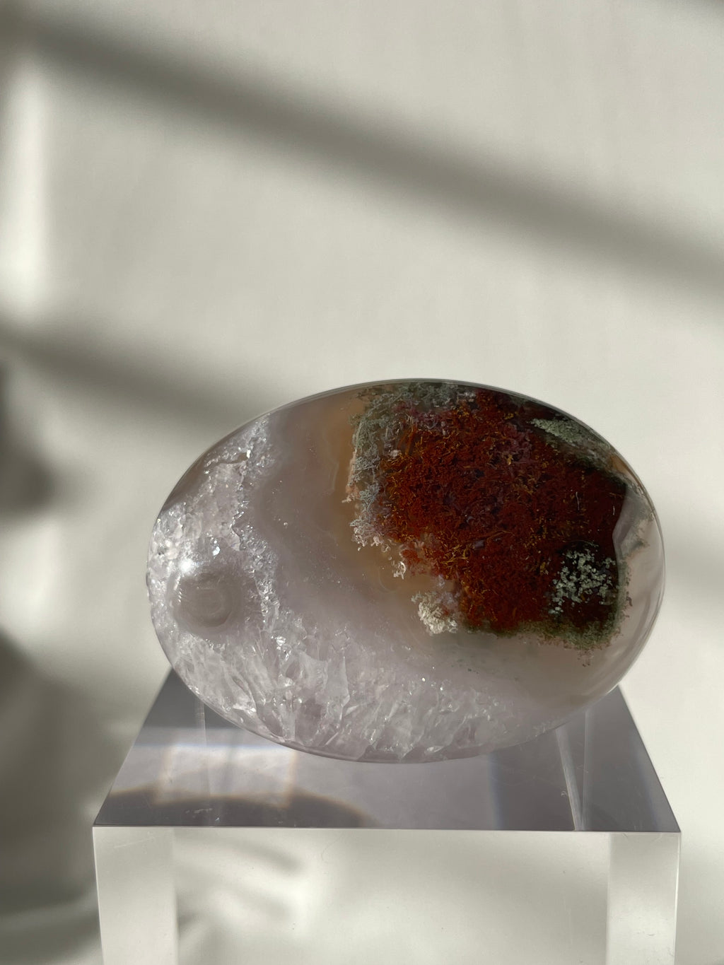 Scenic moss agate palm stone with earthy tones displayed on a clear pedestal, showcasing its natural beauty.