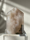 Scenic moss agate tower with soft hues and natural patterns, displayed on a clear pedestal.