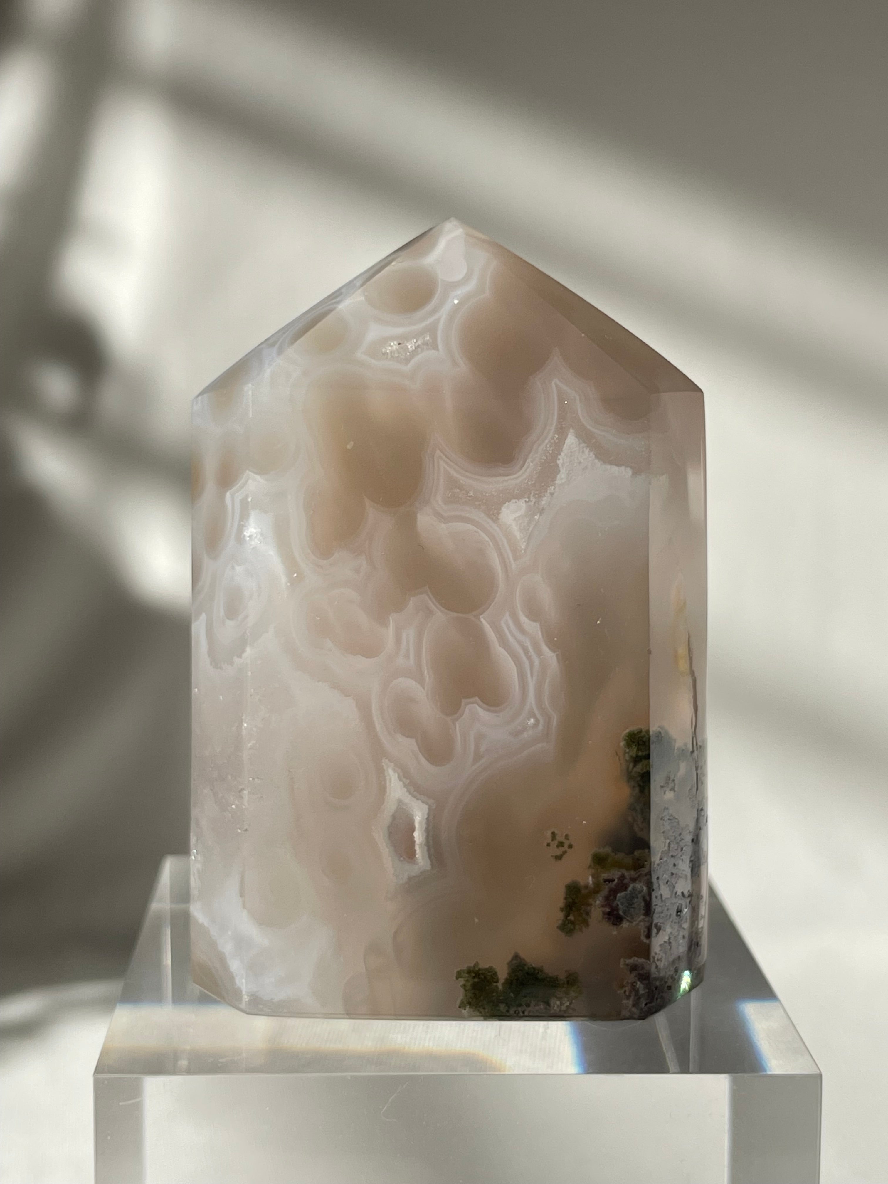 Scenic moss agate tower with soft hues and natural patterns, displayed on a clear pedestal.