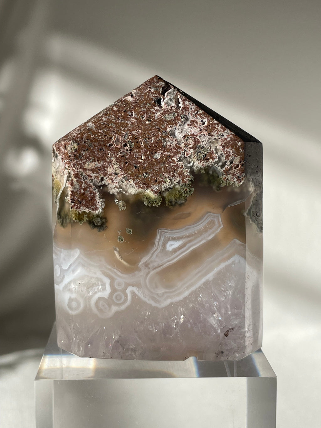 Scenic moss agate tower with earthy tones and unique patterns, displayed on a clear base.