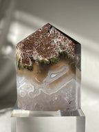 Scenic moss agate tower with earthy tones and unique patterns, displayed on a clear base.