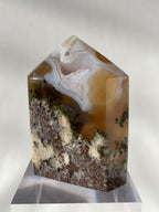 Scenic moss agate tower with earthy tones and unique patterns, displayed on a clear base.