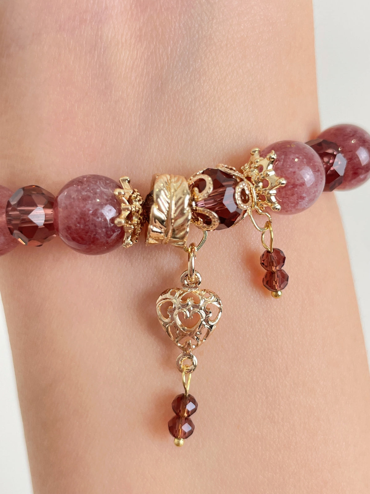 Strawberry quartz bracelet featuring 10mm beads, gold accents, and heart-shaped charm, elegantly displayed on a wrist.