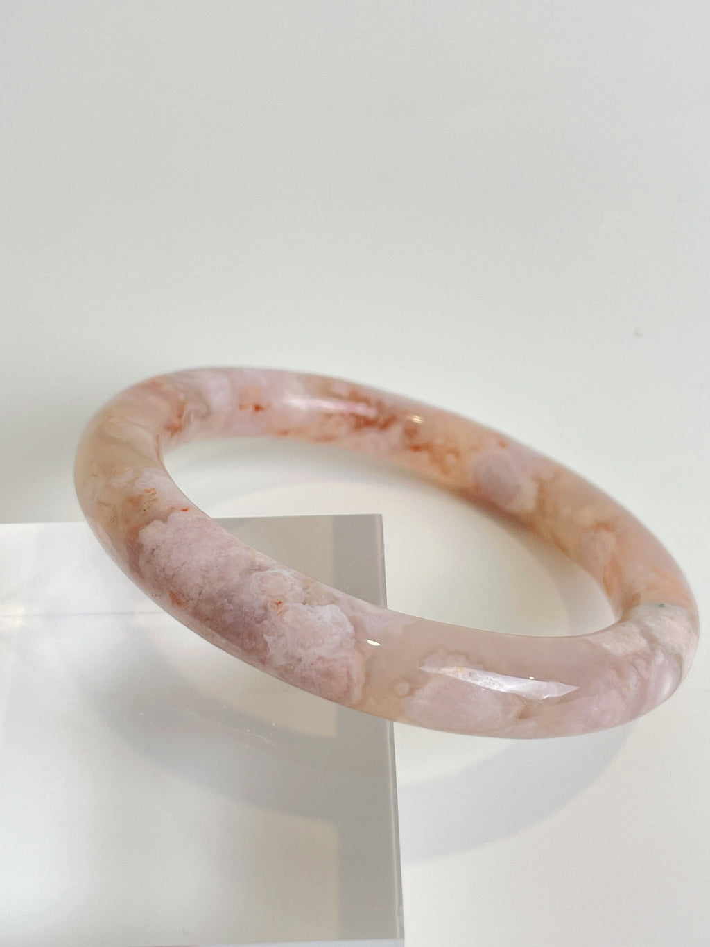 Beautiful flower agate bangle with soft pink hues, displayed on a clear stand, showcasing its smooth finish.