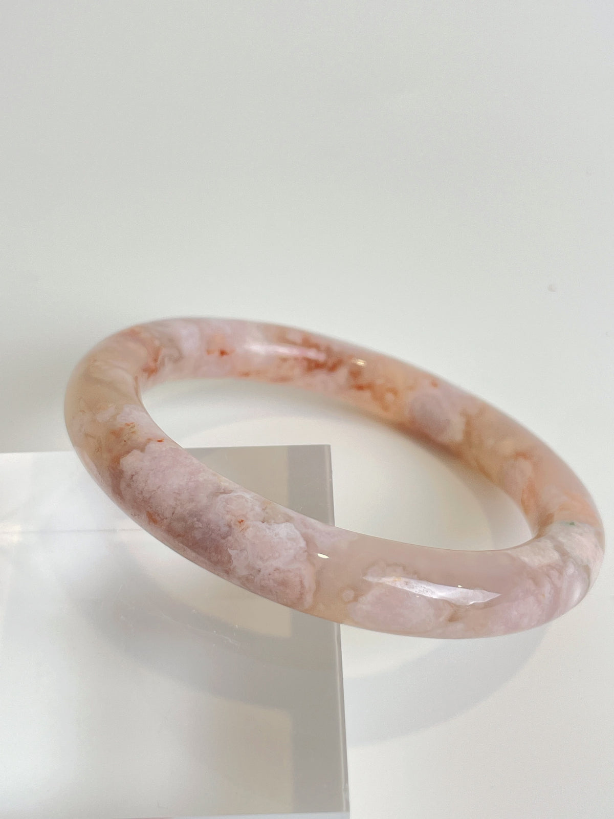 Beautiful flower agate bangle with soft pink hues, displayed on a clear stand, showcasing its smooth finish.