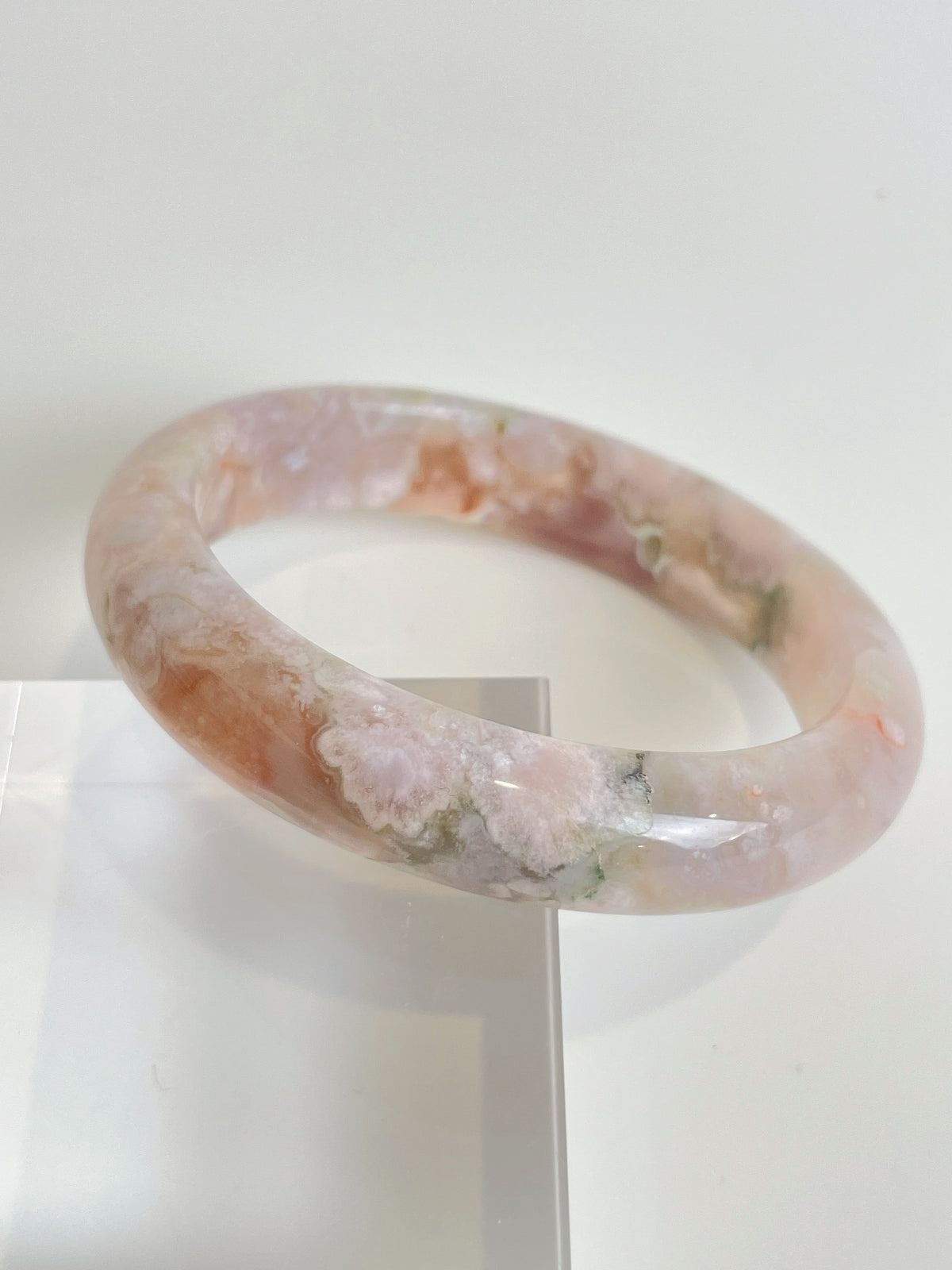 Beautiful flower agate bangle showcasing soft pink and green hues, elegantly displayed on a clear stand.