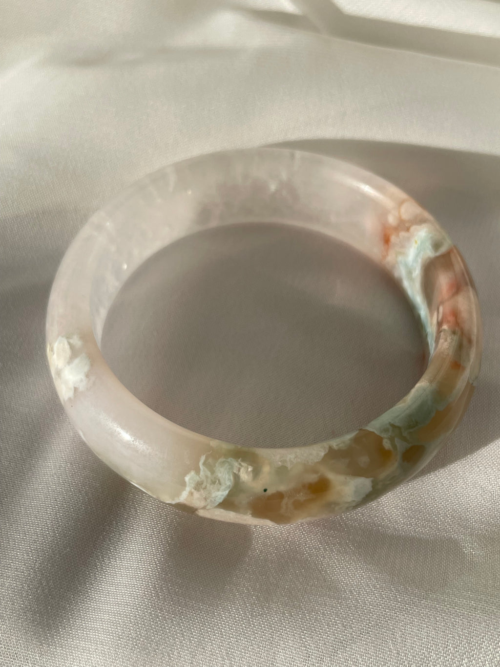 Beautiful flower agate bangle featuring soft pink and earthy tones, resting on a light fabric background.