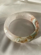 Beautiful flower agate bangle featuring soft pink and earthy tones, resting on a light fabric background.