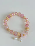 Sakura agate bracelet featuring pink beads, gold accents, and a floral charm, elegantly arranged on a light background.