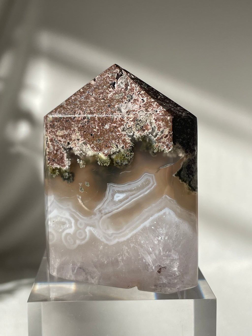 Scenic moss agate tower with earthy tones and unique patterns, displayed on a clear base.