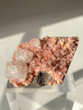 Beautiful pink Heulandite and Apophyllite crystal specimen displayed on a clear stand, showcasing its unique texture and