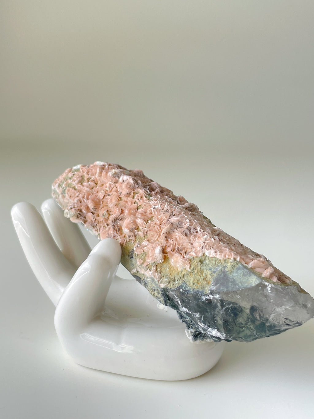 Beautiful pink petal calcite specimen resting on a white hand-shaped display, showcasing its unique texture and colors.