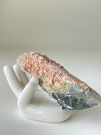 Beautiful pink petal calcite specimen resting on a white hand-shaped display, showcasing its unique texture and colors.