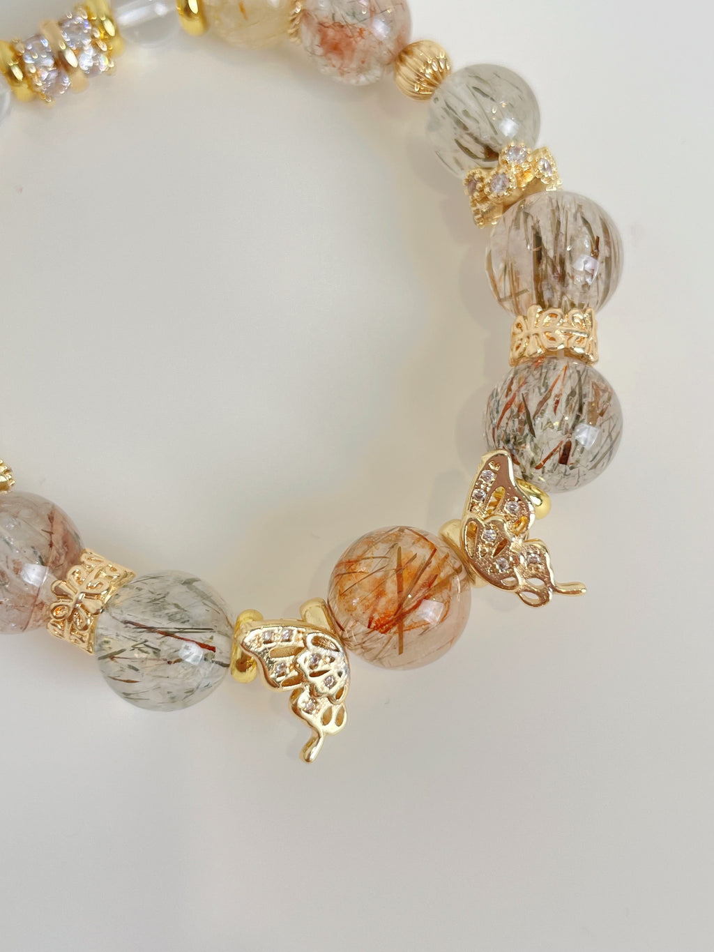 Rutile quartz bracelet featuring 9.5mm beads with gold accents and butterfly charms, showcasing beautiful crystal details.