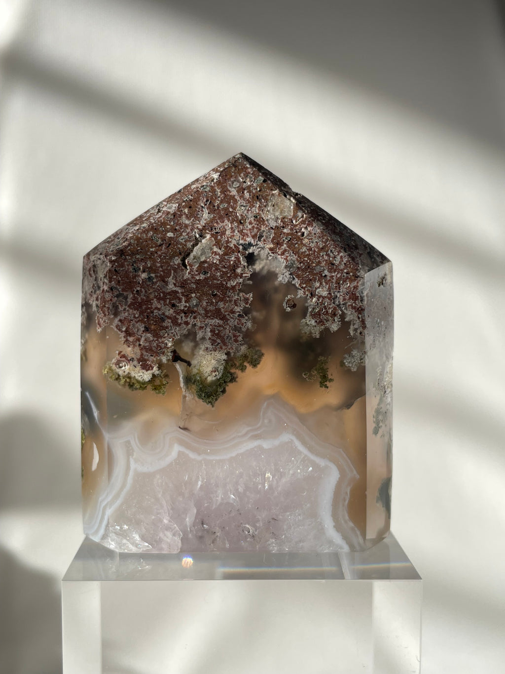 Scenic moss agate crystal tower with earthy tones and unique patterns, displayed on a clear stand.