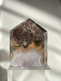 Scenic moss agate crystal tower with earthy tones and unique patterns, displayed on a clear stand.