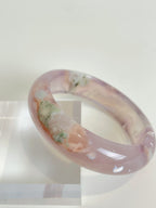 Beautiful flower agate bangle showcasing soft pink and green hues, elegantly displayed on a clear stand.