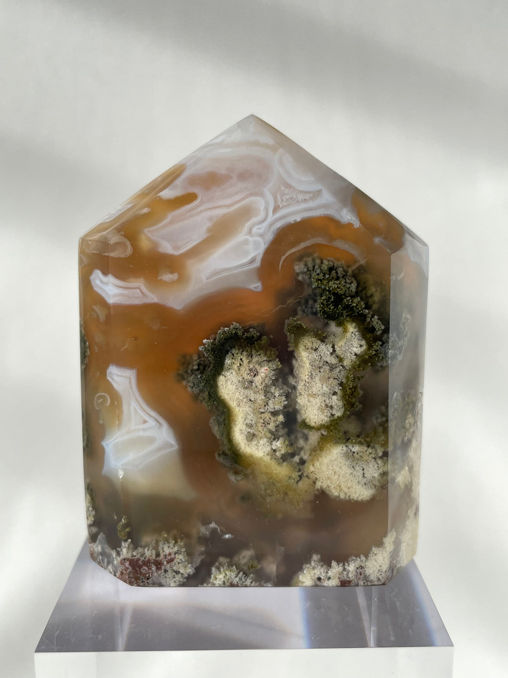 Scenic moss agate tower with earthy tones and intricate patterns, displayed on a clear stand.