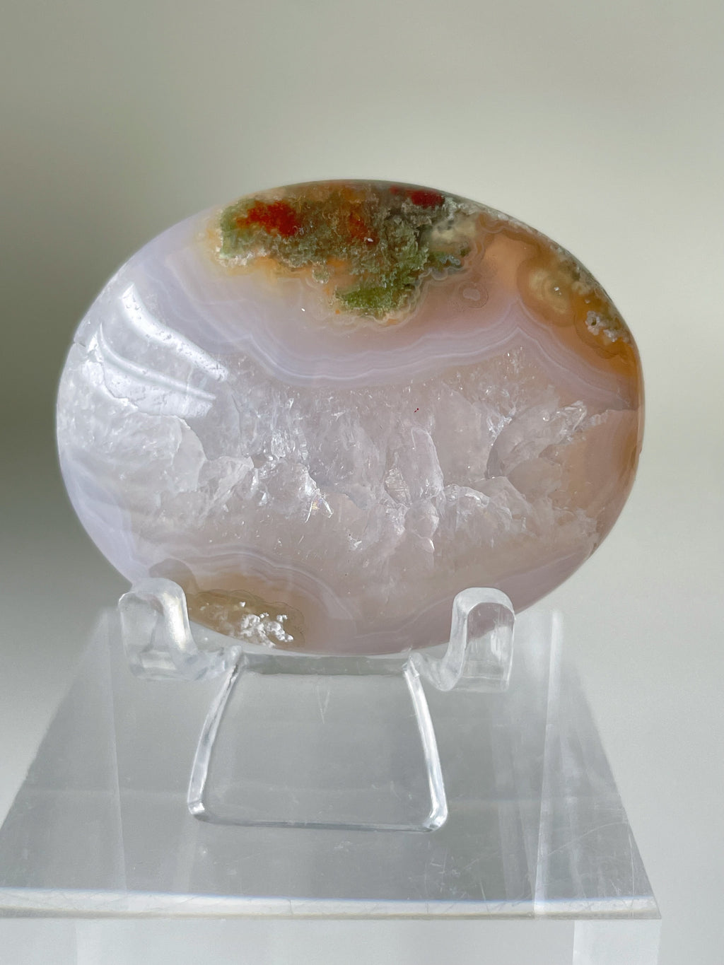 Scenic moss agate palm stone displayed on a clear stand, showcasing natural patterns and earthy colors.