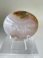 Scenic moss agate palm stone displayed on a clear stand, showcasing natural patterns and earthy colors.