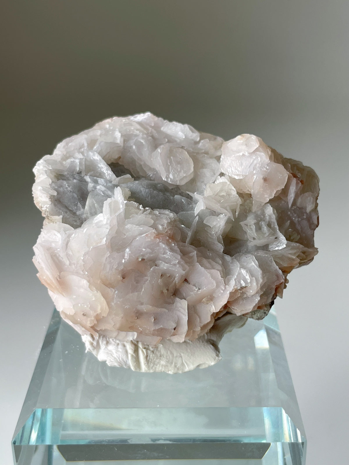 Beautiful pink petal calcite specimen resting on a clear display stand, showcasing its delicate layers and texture.