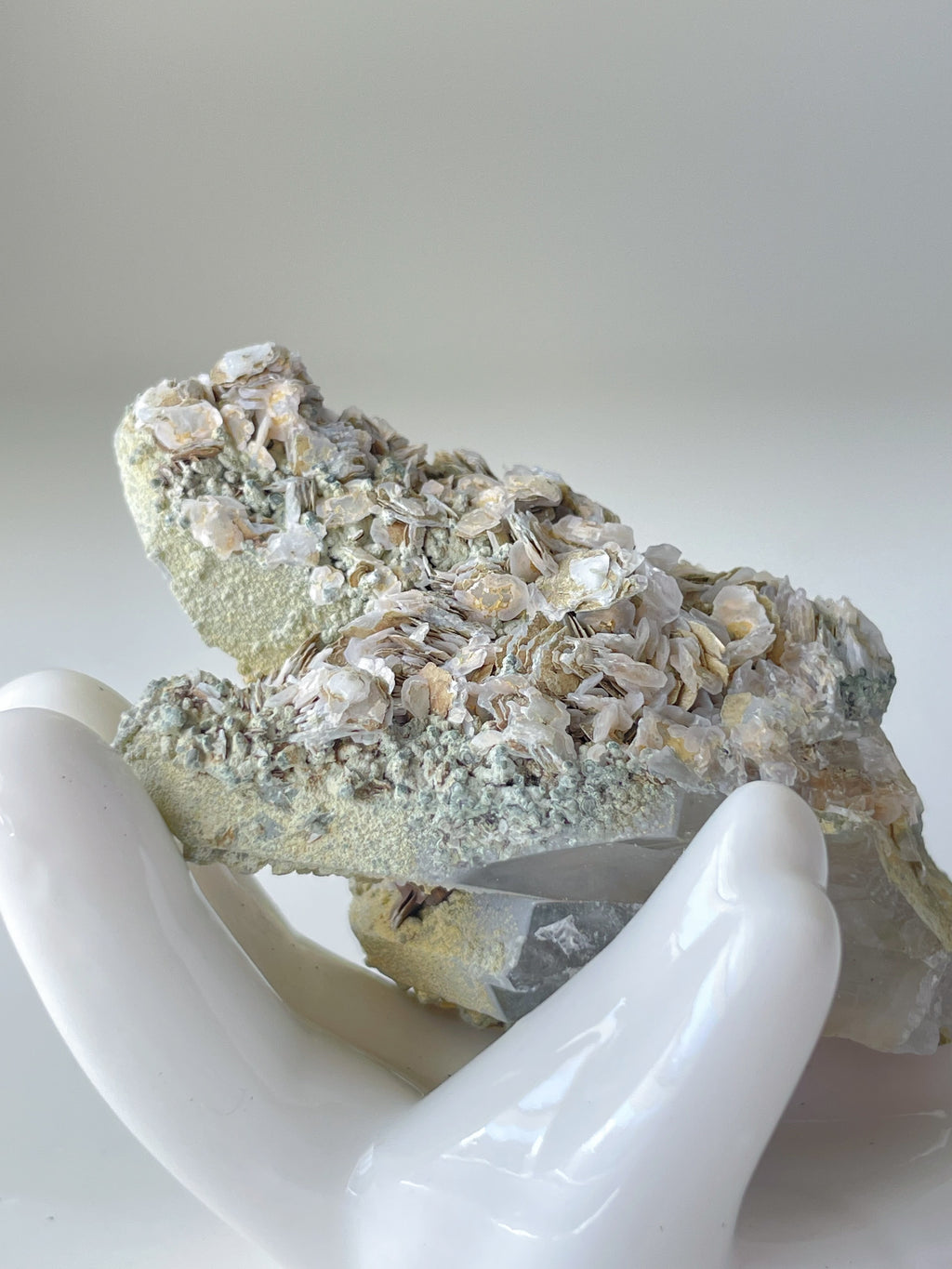 Rosette petal calcite specimen with delicate textures, held gently in a white hand sculpture against a soft background.