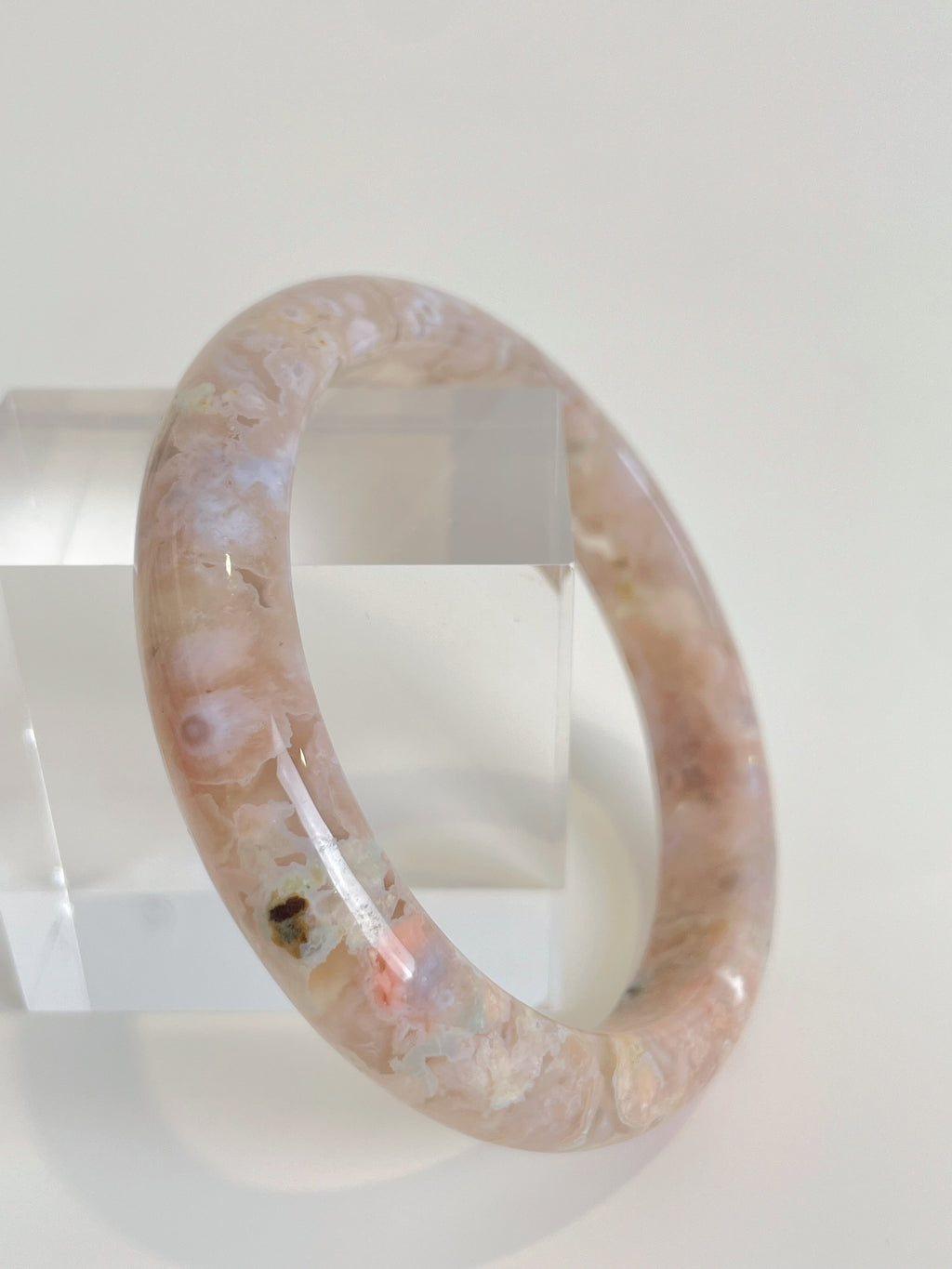 Beautiful flower agate bangle with soft pink hues, displayed on a clear acrylic stand.
