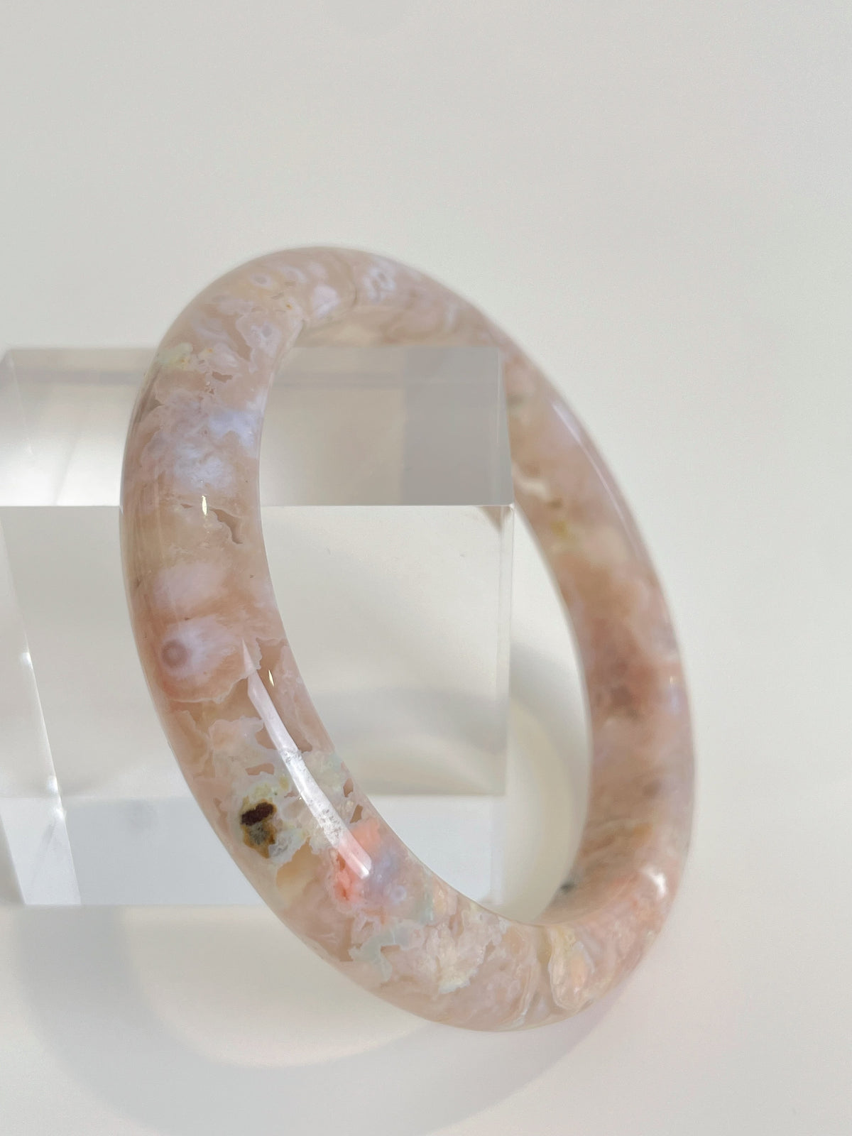 Beautiful flower agate bangle with soft pink hues, displayed on a clear acrylic stand.