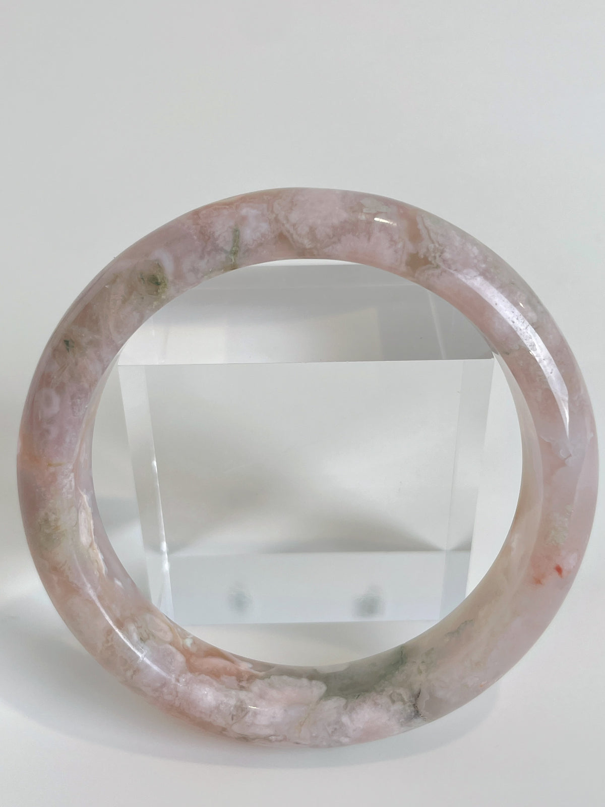 Beautiful flower agate bangle showcasing soft pink hues and subtle green accents, placed beside a clear display block.