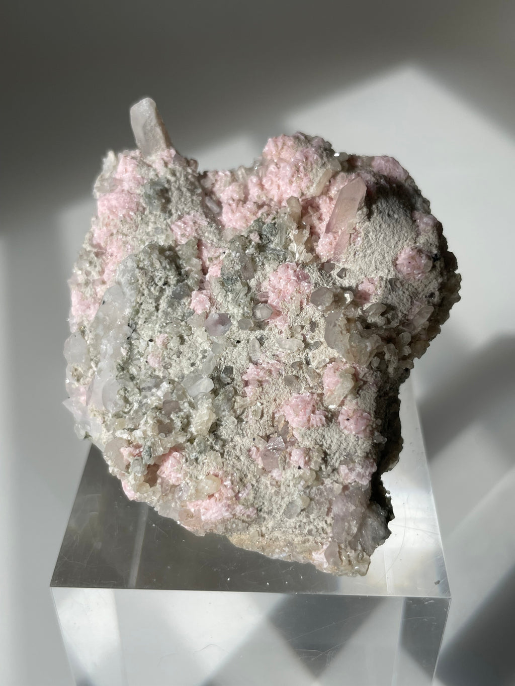 Rhodochrosite cluster with pink and gray hues, displayed on a clear pedestal, showcasing its natural beauty.