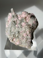 Rhodochrosite cluster with pink and gray hues, displayed on a clear pedestal, showcasing its natural beauty.