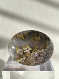 Scenic moss agate palm stone with earthy tones and unique patterns, resting on a clear display stand.