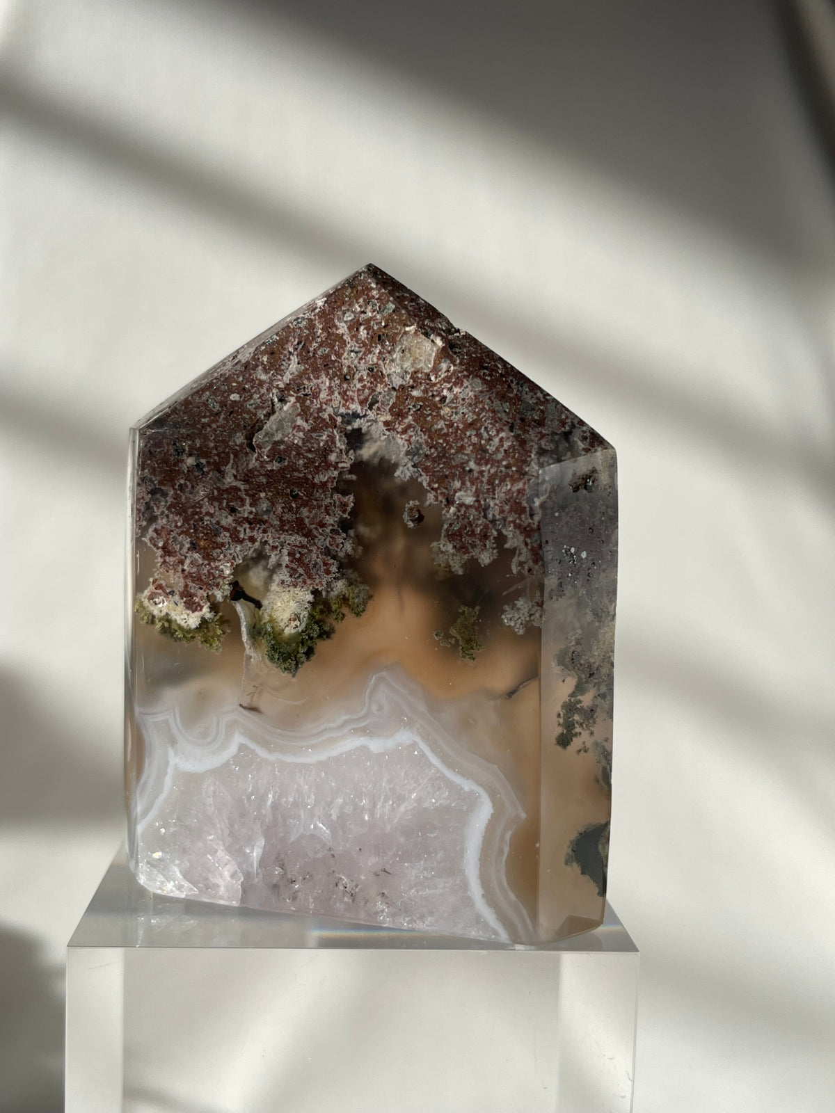 Scenic moss agate tower with earthy tones and unique patterns, displayed on a clear stand.