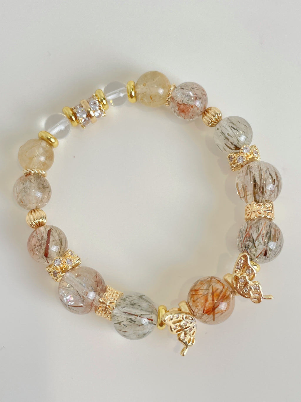 Rutile quartz bracelet featuring 9.5mm beads with gold accents and decorative charms, showcasing a beautiful crystal design.