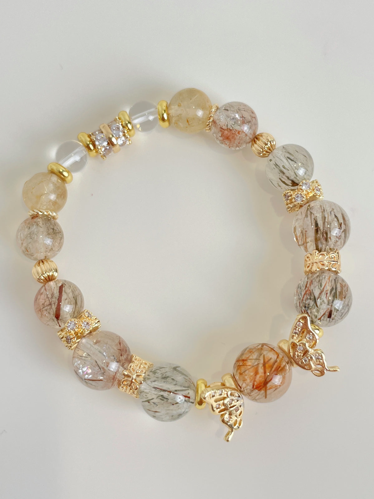 Rutile quartz bracelet featuring 9.5mm beads with gold accents and decorative charms, showcasing a beautiful crystal design.