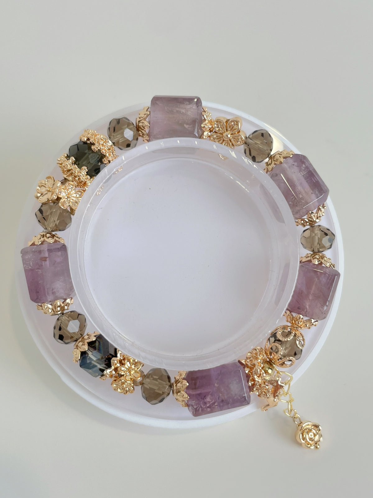 Amethyst cube bracelet featuring pink amethyst and decorative gold accents, elegantly displayed on a clear holder.