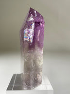 A stunning Brazilian Phantom Amethyst tower with vibrant purple hues and clear facets, displayed on a clear stand.