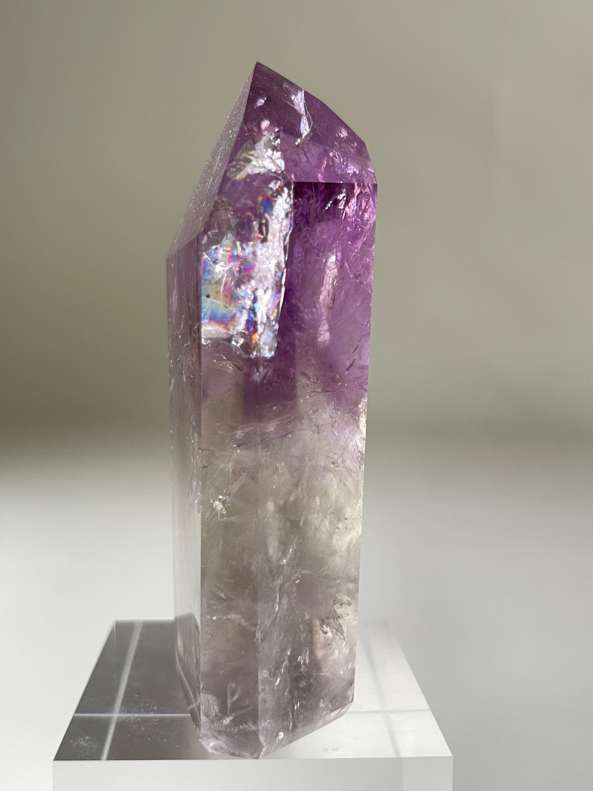 A stunning Brazilian Phantom Amethyst tower with vibrant purple hues and clear facets, displayed on a clear stand.