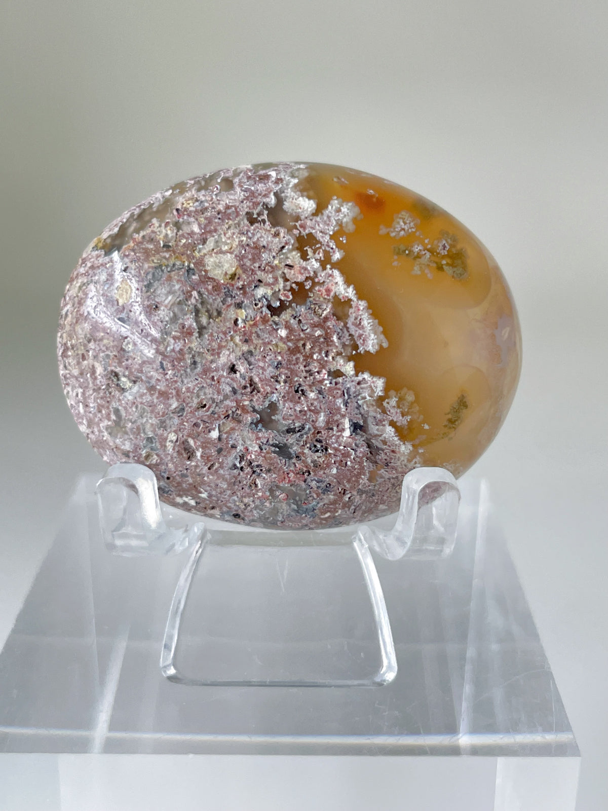Scenic moss agate palm stone displayed on a clear stand, showcasing its unique patterns and warm colors.