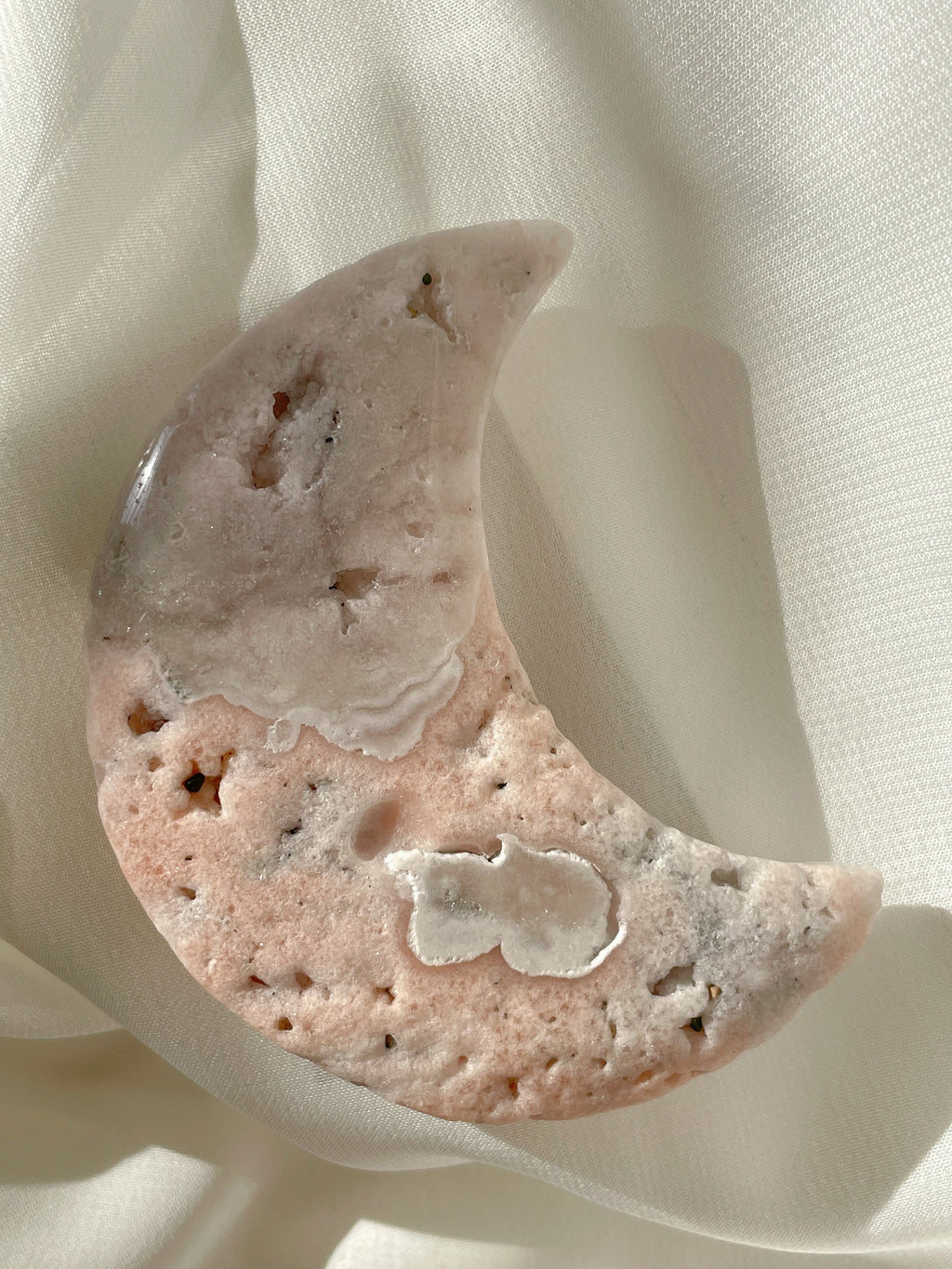 Beautiful flower agate moon with soft pink and white patterns, resting on a light fabric background.