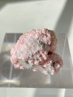 Beautiful rhodochrosite cluster with a pink, textured surface, displayed on a clear stand.