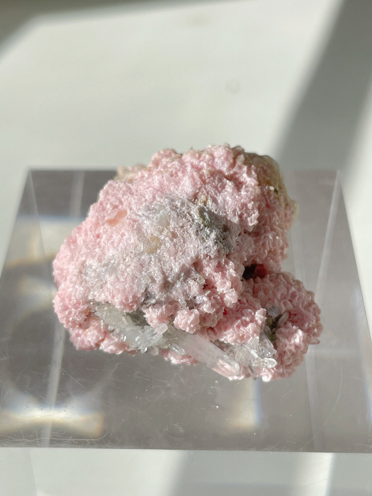 Beautiful rhodochrosite cluster with a pink, textured surface, displayed on a clear stand.