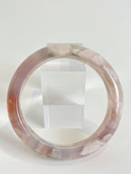 Beautiful flower agate bangle showcasing soft pink hues and natural patterns, displayed beside a clear crystal stand.