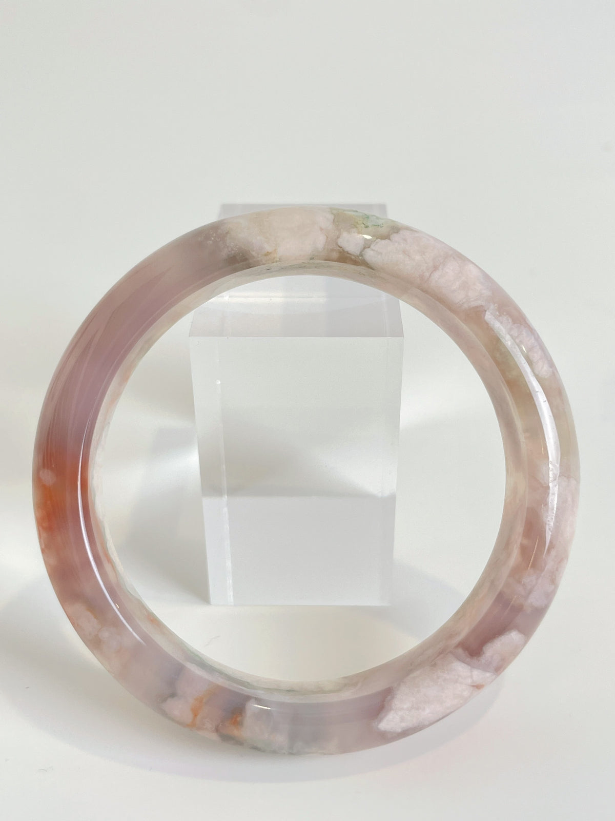 Beautiful flower agate bangle showcasing soft pink hues and natural patterns, displayed beside a clear crystal stand.