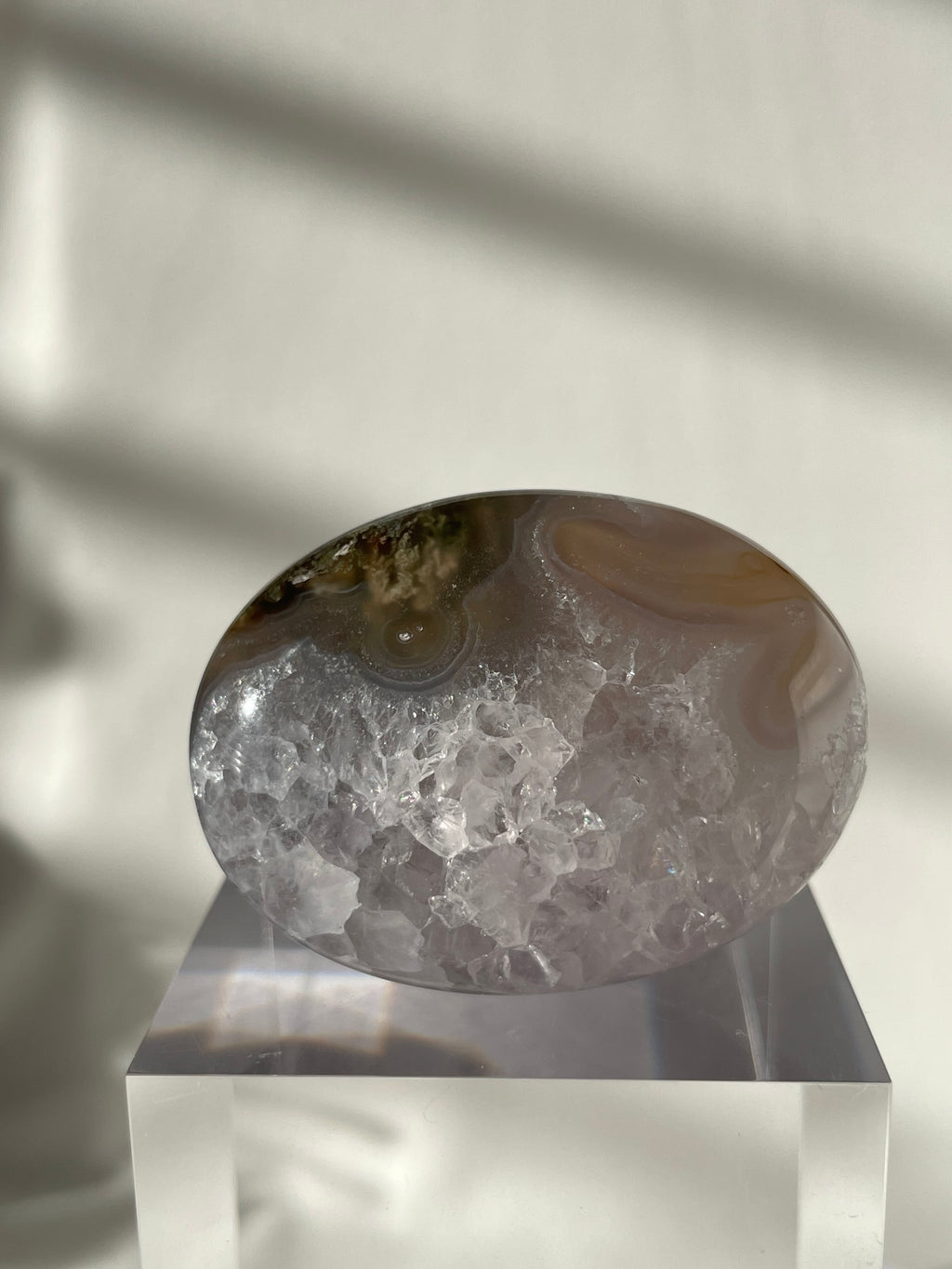 Scenic moss agate palm stone with unique patterns, displayed on a clear pedestal against a softly lit background.