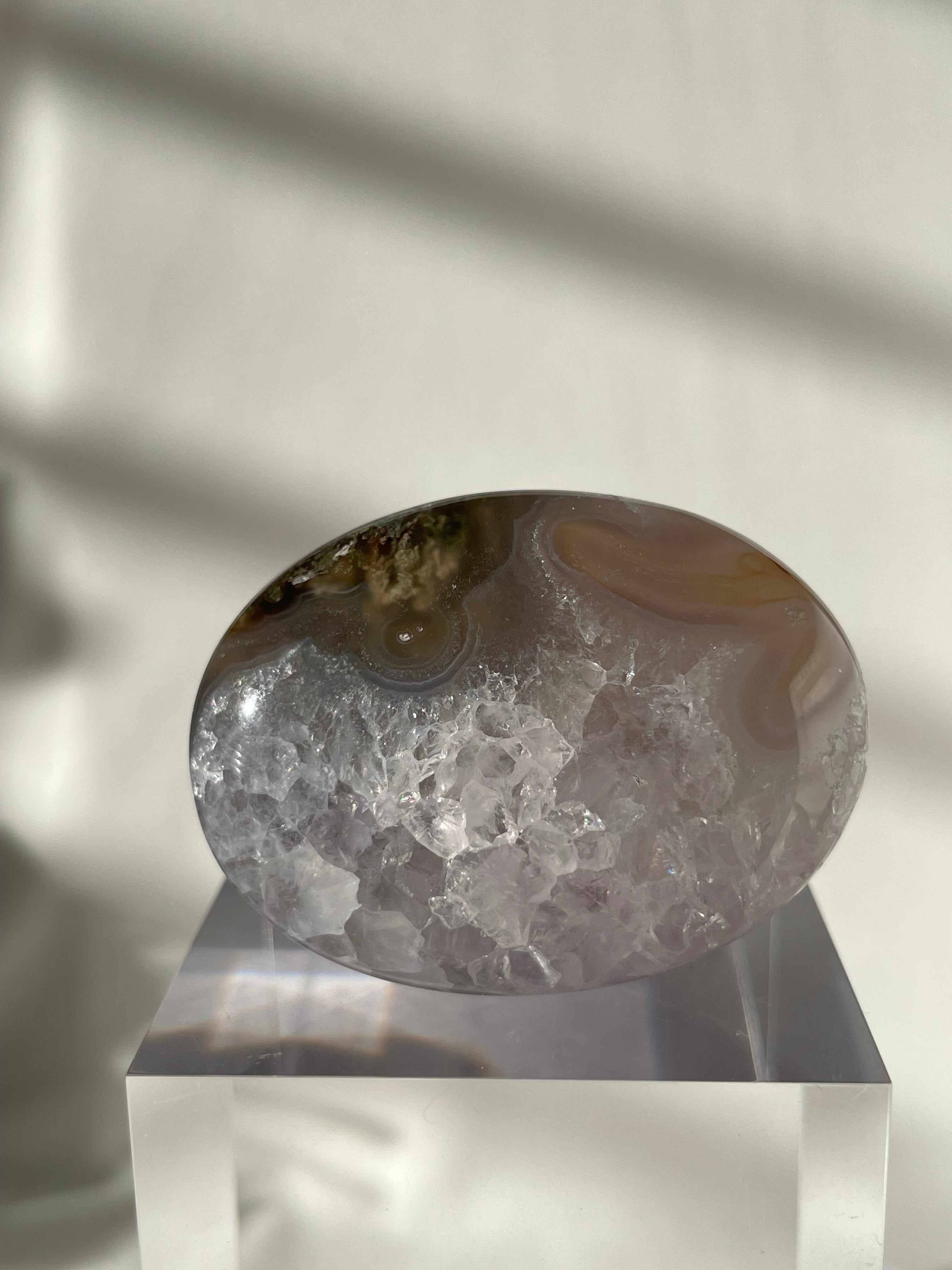 Scenic moss agate palm stone with unique patterns, displayed on a clear pedestal against a softly lit background.