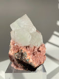 Beautiful pink Heulandite and Apophyllite crystal specimen displayed on a clear pedestal, showcasing natural textures.