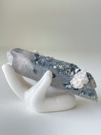 A stunning pink petal calcite specimen resting on a white ceramic hand display, showcasing its unique crystal formations.